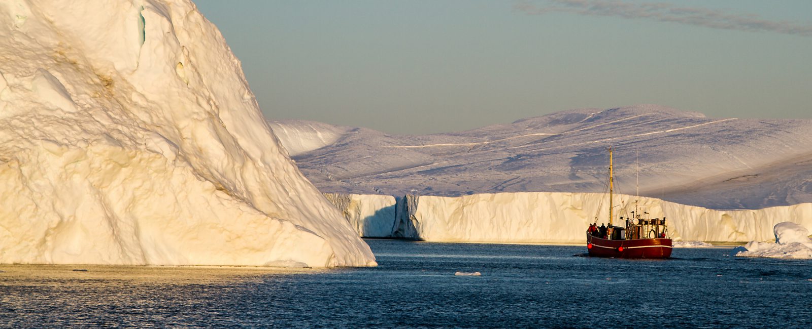 Boot vor riesigen Eisbergen in der Abendsonne